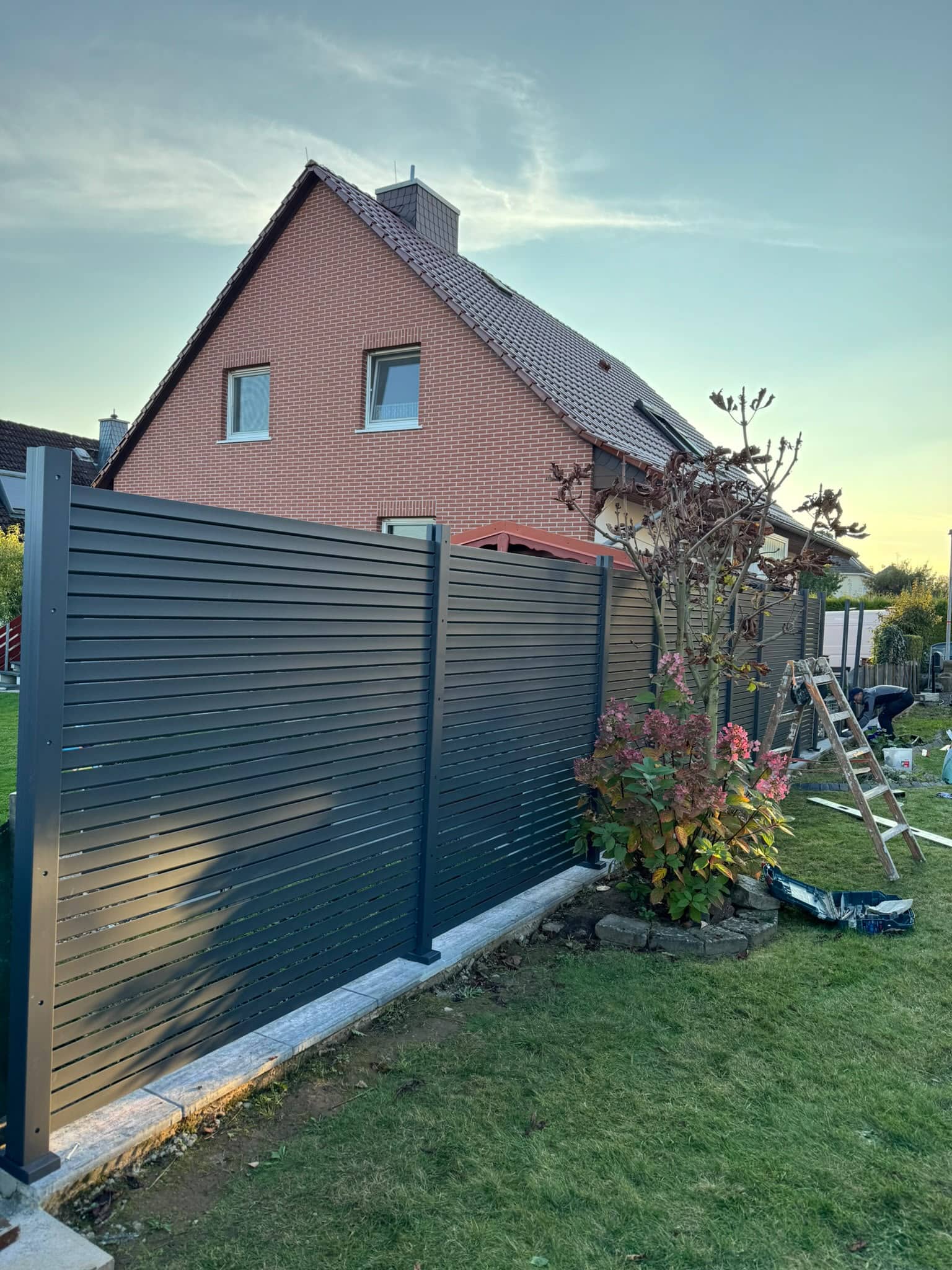 Moderner Aluzaun mit horizontalen Lamellen in Anthrazit vor Einfamilienhaus