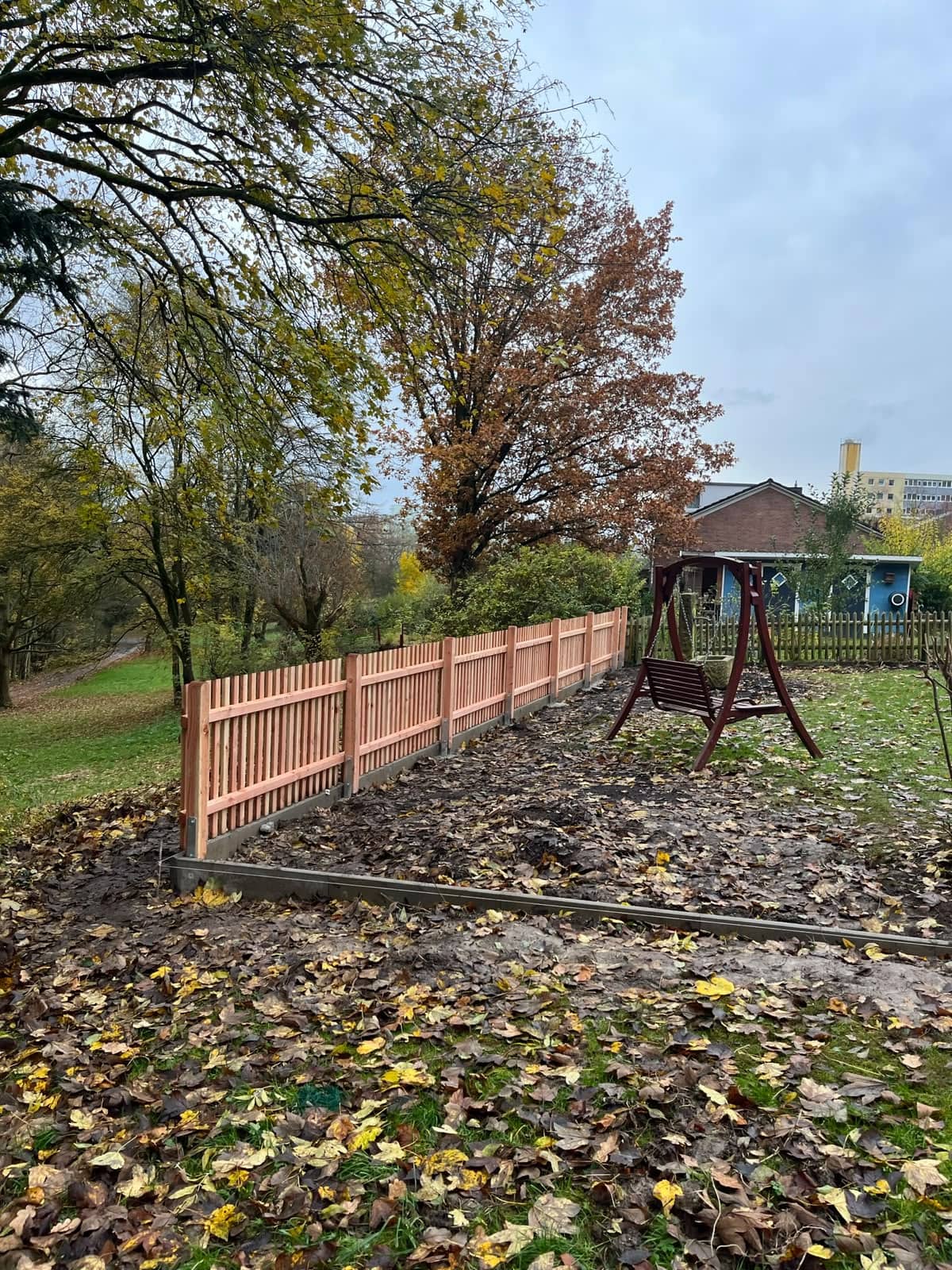 Frisch montierter Holz-Lattenzaun im herbstlichen Garten mit Schaukel